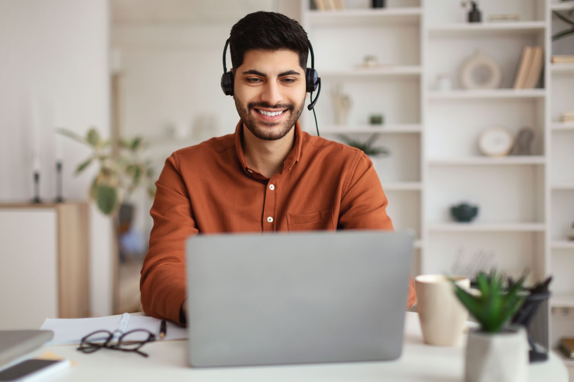 man sitting at table, using laptop and headset